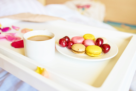 Side view of cup of coffee with tasty colorful macarons or macaroons on white tray. Romantic breakfast conceptの写真素材