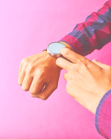 Man wear smart watch in everyday lifestyle with blank screen. Concept business, omnichannel, multi payment, lifestyle using. Smartwatch - modern gadget with empty display, copy space. Pink backgroundの写真素材