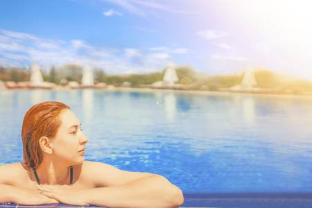 Cute female swimming in the pool. Young pretty woman relaxing in the water,  looks out of the pool, hanging on the railing. Copy space for textの写真素材
