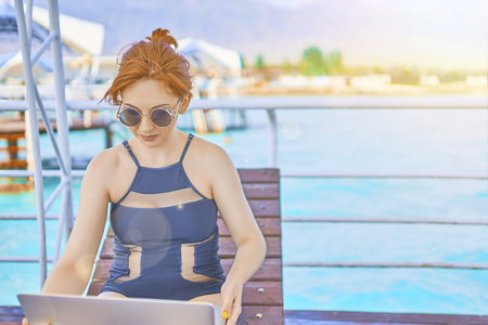 Redhead girl working with a laptop on the sea. Female freelancer working on the beach. Attractive hair woman using laptop on the beach and look to the laptop.の写真素材