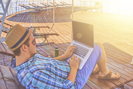 A man on vacation, sits on the pier and works.の写真素材