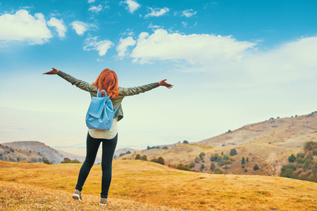 Pretty woman with blue backpack outdoors enjoying nature mountains and arms outspread in celebration of a beautiful sunny summer day and freedomの写真素材
