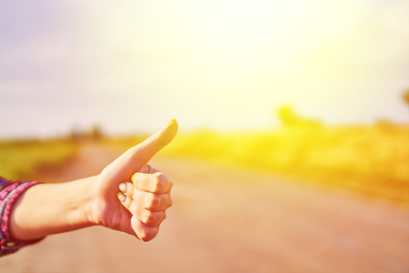 Hand of woman traveler with thumbs up form the asphalt road go to travel at sunny dayの写真素材
