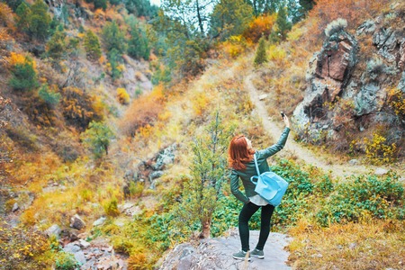 Sexy female hiker posing for selfie in mountains forest. Woman with a backpack is standing on a big stone in the mountains in the forest and vlogging for her channel.の写真素材
