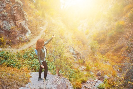 Cute female hiker taking selfie or making live video stream vlog in mountains forest. Woman tourist with a backpack is walking along a path in the woods in the mountains.の写真素材