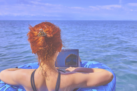 Young woman is floating on the sea in a swimming circle. A girl is relaxing on the sea on the inflatable ring with minicomputer.の写真素材