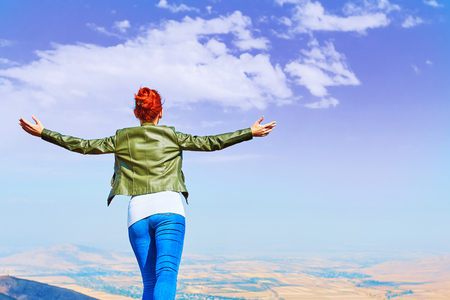Image of a girl in a field standing in the distance with her back to the camera and her arms outspread in celebration of a beautiful sunny summer day and freedomの写真素材