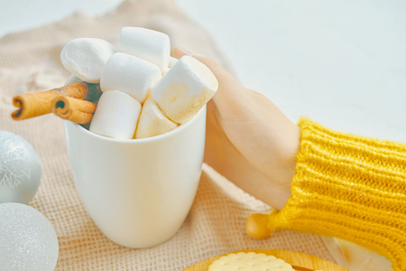 Woman drinking hot chocolate with marsmallows and cinnamon next to Christmas toys while decoratingの写真素材
