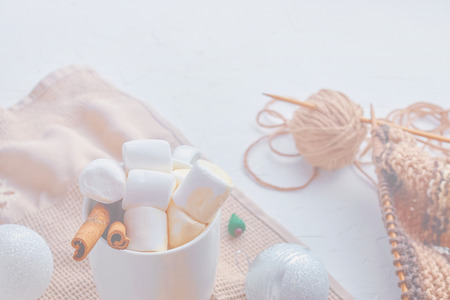 Cocoa with cookies, marshmallows, Christmas decorations, miniature Christmas tree and scarf knitting tools on the tableの写真素材