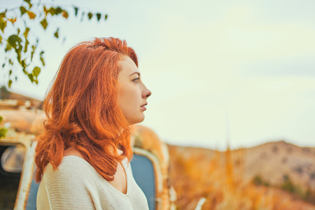 Woman sitting on rusty old classic truck. Portrait of a beautiful woman admires of sunset in autumn.の写真素材