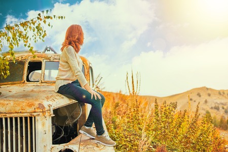 Woman sitting on rusty old classic truck. Young woman in a summer field sitting on old car.の写真素材