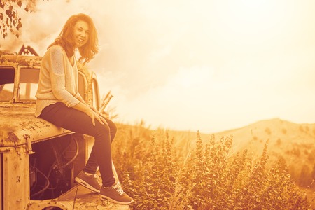 Woman sitting on rusty old classic truck. A woman admires the sunset on an autumn field.の写真素材
