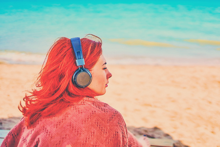 Pretty woman listening to music on the beach. Woman on vacation sunbathes on the beach, and listens to relaxing music.の写真素材