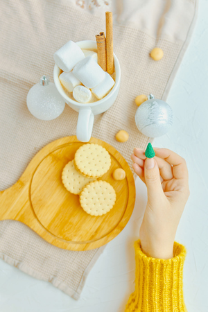 Woman in a yellow sweater holding a miniature Christmas tree with festive toys, coffee and cookies on the tableの写真素材