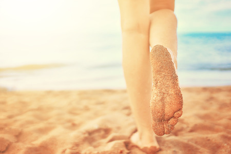 In the frame of a woman feet walking on the beach by the sea on a Sunny day in a tropical hotel on vacationの写真素材