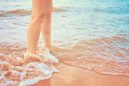 In the frame of a woman feet walking on the beach by the sea on a Sunny day in a tropical hotel on vacation. Waves of ocean wash her feetの写真素材