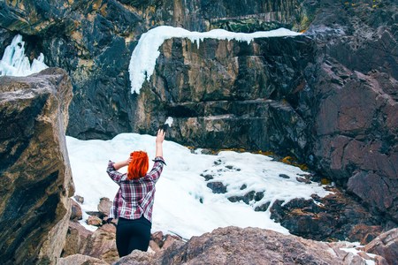 Freedom traveler woman standing. with raised arms and enjoying a beautiful frozen waterfall