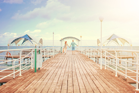 Young couple resting on the beach on their honeymoon. Man and woman holding hands on pier at seaの写真素材