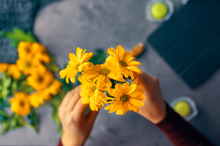 Woman puts a yellow chrysanthemum flowers in a glass transparent vase on the loft tableの写真素材