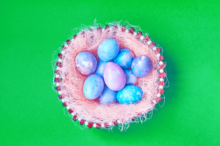 Group of Easter eggs with space galactic pattern in a basket with a filler in the form of a pink nest on a green background. flat layの写真素材