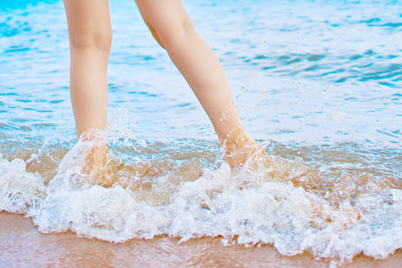In the frame of a woman's feet walking on the beach by the sea on a Sunny day in a tropical hotel on vacation. Waves of ocean wash her feetの写真素材