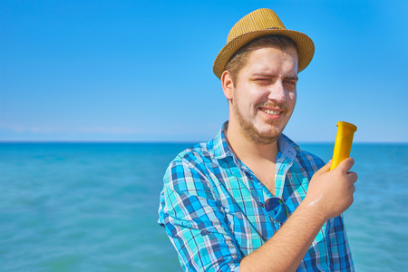 Guy putting onsun protection lotion on the face. A man by the sea, his face smeared with sunscreen.の写真素材