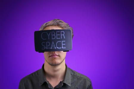 Young man in a shirt uses virtual reality glasses with the inscription "cyberspace" on them in front of a proton purple backgroundの写真素材
