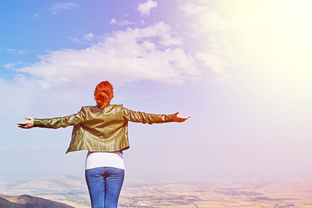Beauty woman outdoors enjoying nature. Image of a girl in a field standing in the distance with her back to the camera and her arms outspread in celebration of a beautiful sunny summer day and freedomの写真素材