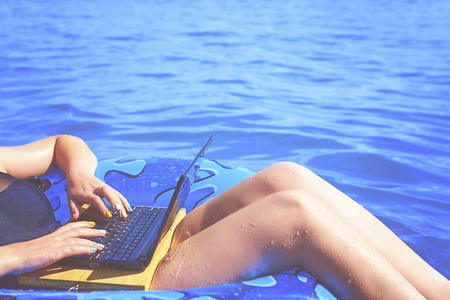 A young woman is floating on the sea in a swimming circle. A girl is relaxing on the sea on the inflatable ring with minicomputer.の写真素材