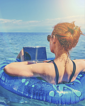 Beautiful young woman with on donuts and a desktop computer relaxing in the ocean.の写真素材