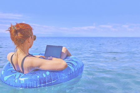 Beautiful young woman with on donuts and a desktop computer relaxing in the ocean.の写真素材