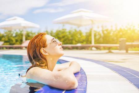 Young Woman in sunglasses Leaning On The Edge Of swimming pool at spa resort. Relaxing concept.の写真素材