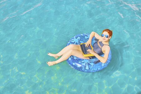Workaholic woman working on vacation, the concept of remote work. Business woman sitting in a inflatable ring at sea and using laptop.の写真素材