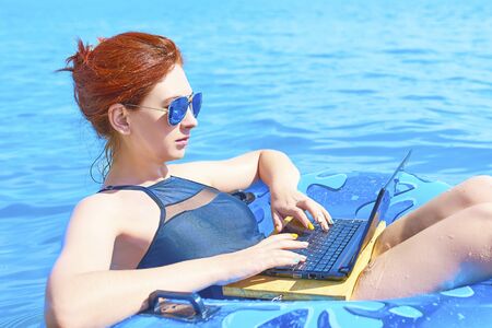 Beautiful young woman with on donuts and a desktop computer relaxing in the ocean.の写真素材