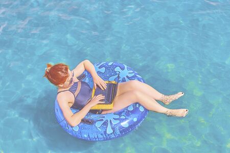 A young woman is floating on the sea in a swimming circle. A girl is relaxing on the sea on the inflatable ring with minicomputer.の写真素材
