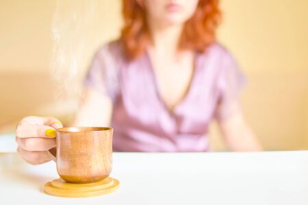 Cute woman in a purple silk robe drinking coffee early in the morning in bed. White cup of latte on the tray. Breakfast conceptの写真素材