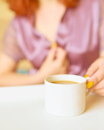 Cute woman in a purple silk robe drinking coffee early in the morning in bed. White cup of latte on the tray. Breakfast conceptの写真素材