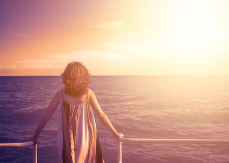 Behind girl on pier. Vintage photo of relaxing young woman on pier at the lake in sunset.の写真素材