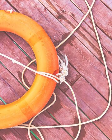 Orange lifebuoy with rope on a wooden pier near sea. Close up of lifebuoy on wooden pier at the beach.の写真素材