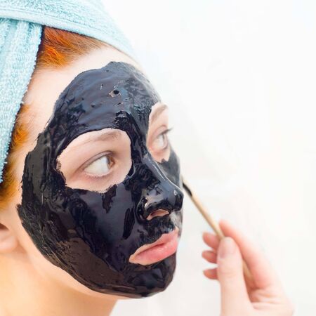 Woman in bathroom to put on cosmetic black mask on white background, right view. Sunny day. Put yourself in order.の写真素材
