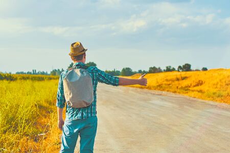 Hitchhiker with backpack in summer hat, light shirt, shorts on the road in tropical country in Sunny weather at autumnの写真素材