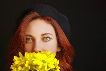 French redhead woman in black beret holds and sniffs yellow chrysanthemumsの写真素材