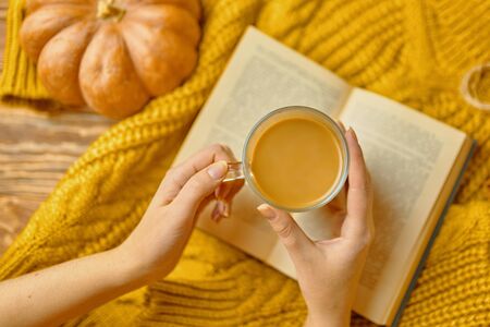 Yellow coffee Cup and old book on wooden background with autumn leaves and pumpkins.の写真素材