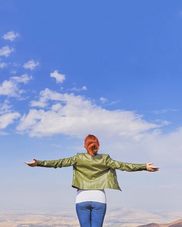 Beauty woman outdoors enjoying nature. Image of a girl in a field standing in the distance with her back to the camera and her arms outspread in celebration of a beautiful sunny summer day and freedomの写真素材