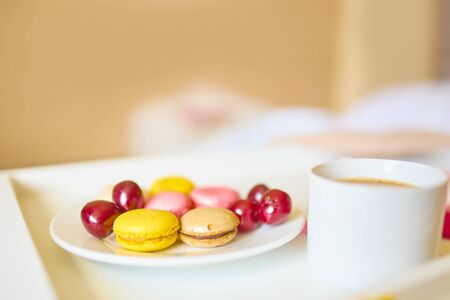 Side view of cup of coffee with tasty colorful macarons or macaroons on white tray. Romantic breakfast conceptの写真素材