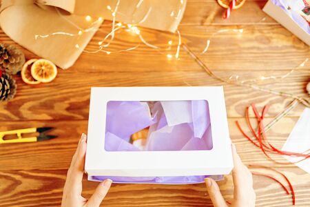 New year packaging on decorated festive table with sparkle stars on wooden background. Woman hands holding christmas gift box.の写真素材