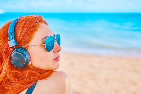 Handsome woman listening to music on the beach. Young female using and wearing headphones on the beach.の写真素材