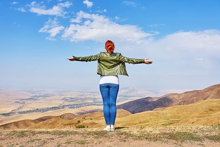 Beauty woman outdoors enjoying nature. Image of a girl in a field standing in the distance with her back to the camera and her arms outspread in celebration of a beautiful sunny summer day and freedomの写真素材