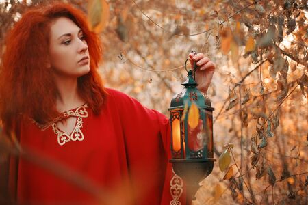 Woman in red holding a lantern with a candle. The candle burns inside the lantern which is in the hands of a womanの写真素材
