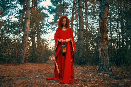 Woman in red holding a lantern with a candle. Hand lantern with a candle shines in the woods.の写真素材